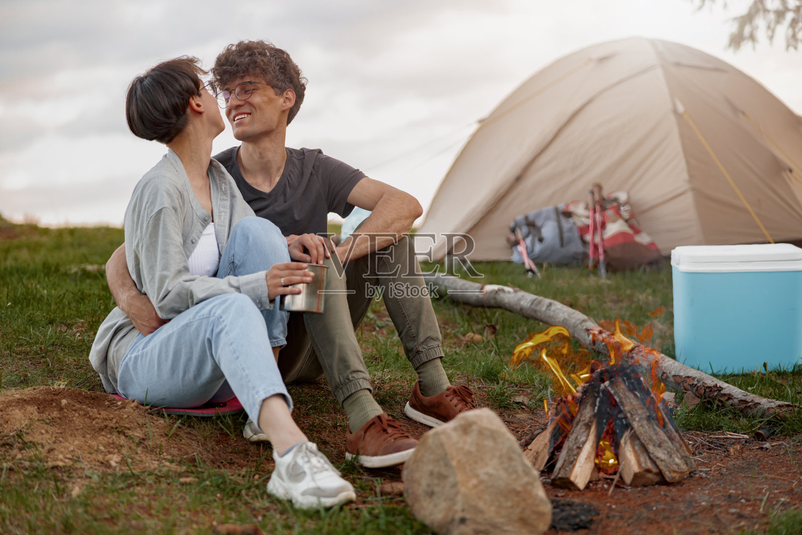 一对快乐的高加索游客在帐篷旁的篝火旁拥抱着。夏季露营。照片摄影图片