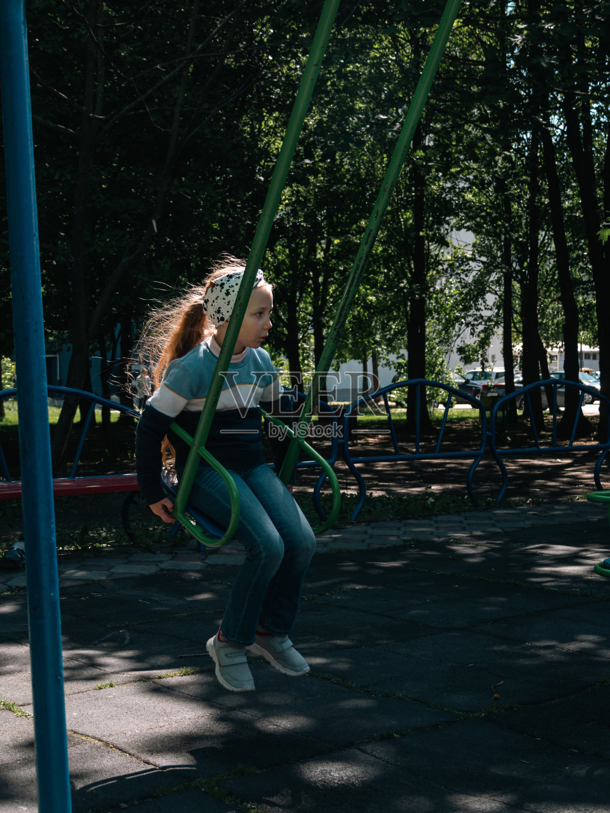 快乐的孩子在春天的公园里荡秋千。可爱的长发小女孩独自在操场的树荫下荡秋千照片摄影图片