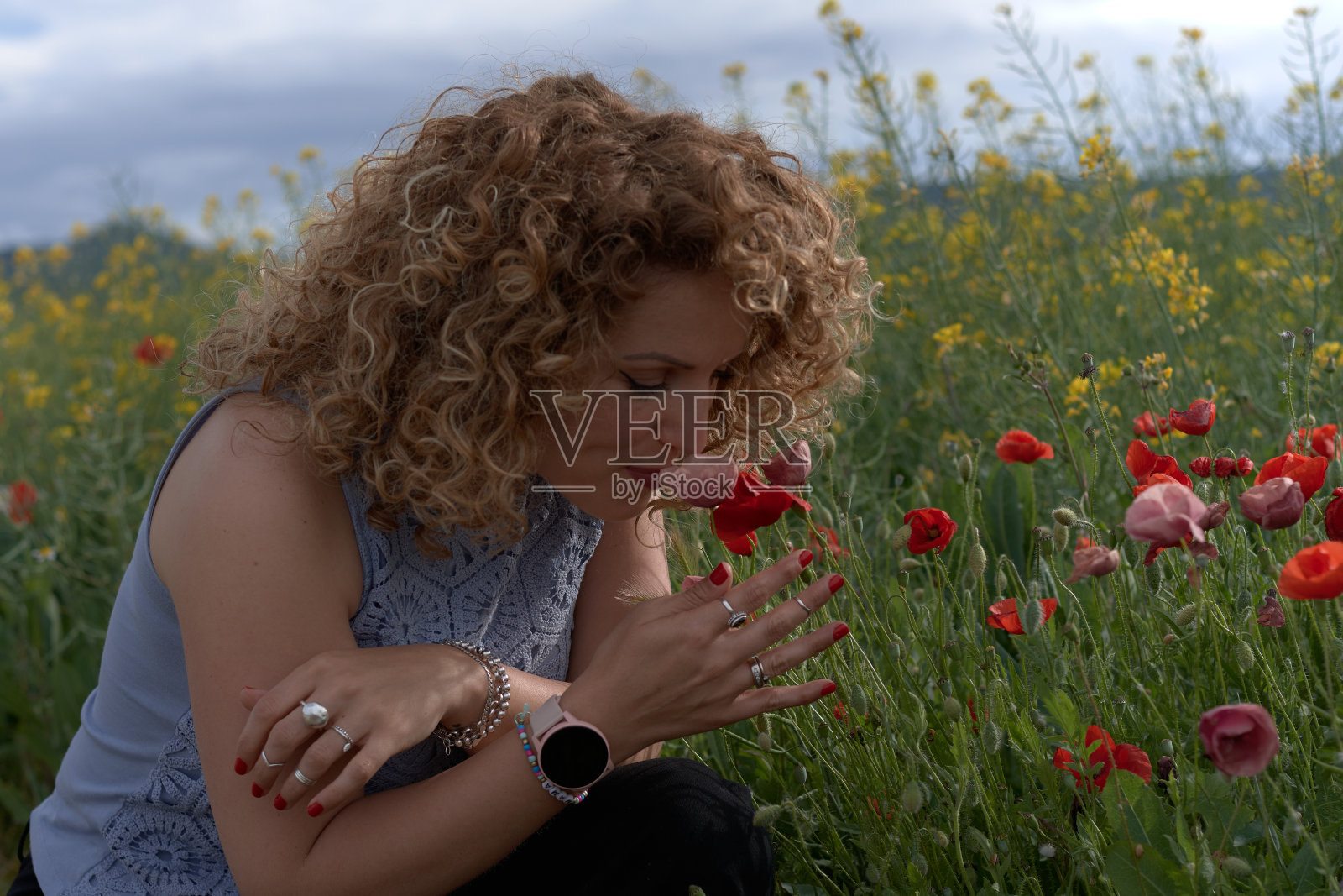 一个年轻的女人闻到了田野里的一朵红花照片摄影图片