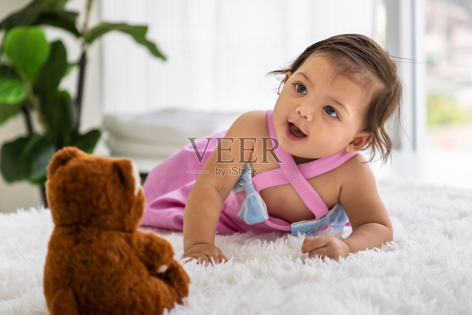 亚洲小女孩带着泰迪熊娃娃在家里的地毯上爬行。新生儿在床上放松。幼儿托儿所。照片摄影图片