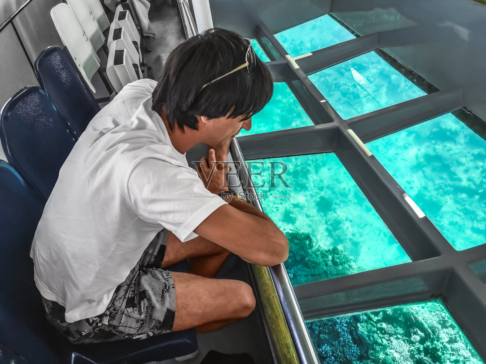 一名男子透过深海潜水器透明的底部观察红海深处的海底生活照片摄影图片