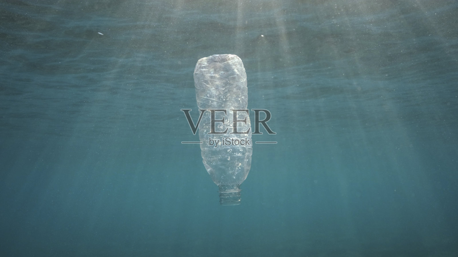 塑料污染：废弃塑料瓶在日落时分的阳光下漂浮在水面。照片摄影图片