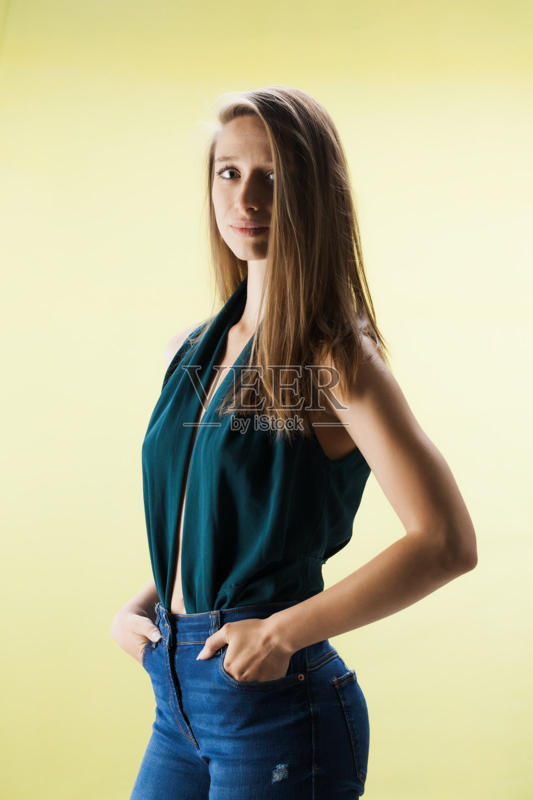 美丽的女孩在黄色的背景下。深色头发的女士穿着漂亮的衬衫和牛仔裤在摄影棚里摆拍……照片摄影图片