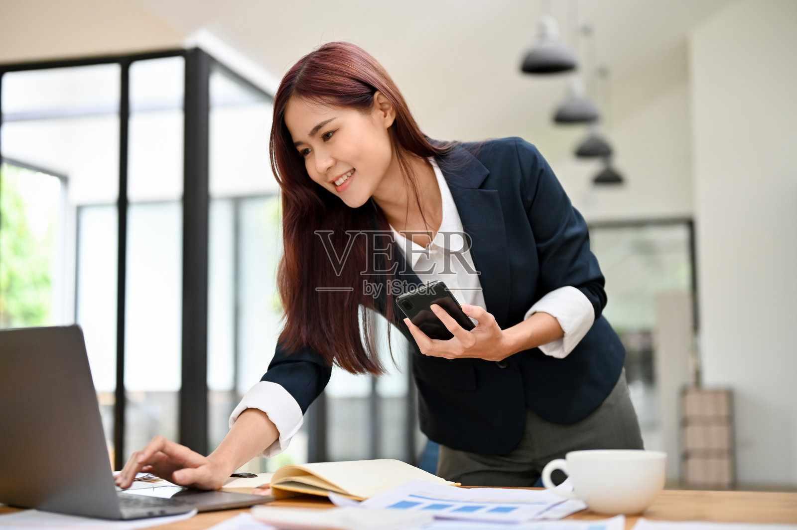 成功的亚洲女商人在她的办公桌上靠在笔记本电脑上工作。照片摄影图片