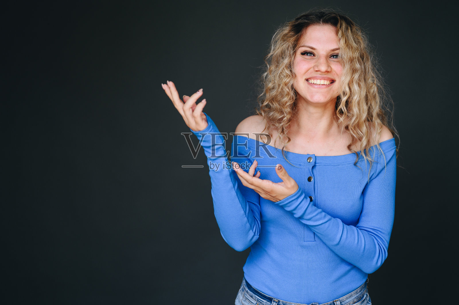 穿着蓝色上衣的卷发快乐女孩的肖像。用手指向背景上的空白区域照片摄影图片