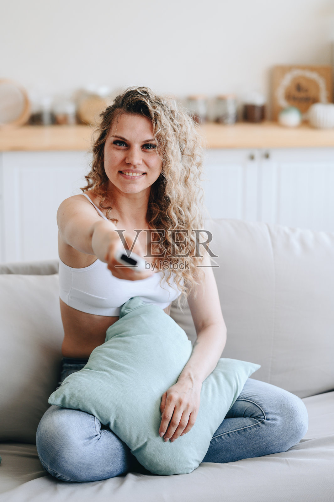 一个穿着白色运动上衣的女孩的垂直照片。女孩通过开关遥控器看电视。照片摄影图片