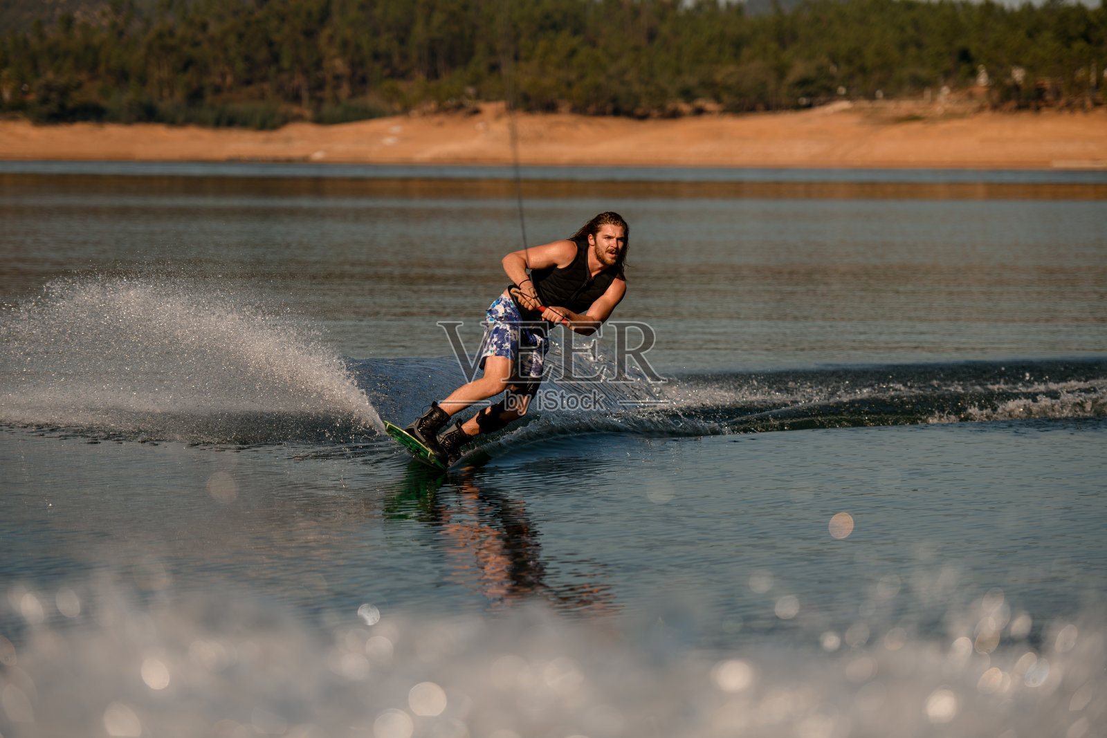 健壮的大胡子握着绳子，熟练地在河上玩水上滑板。照片摄影图片