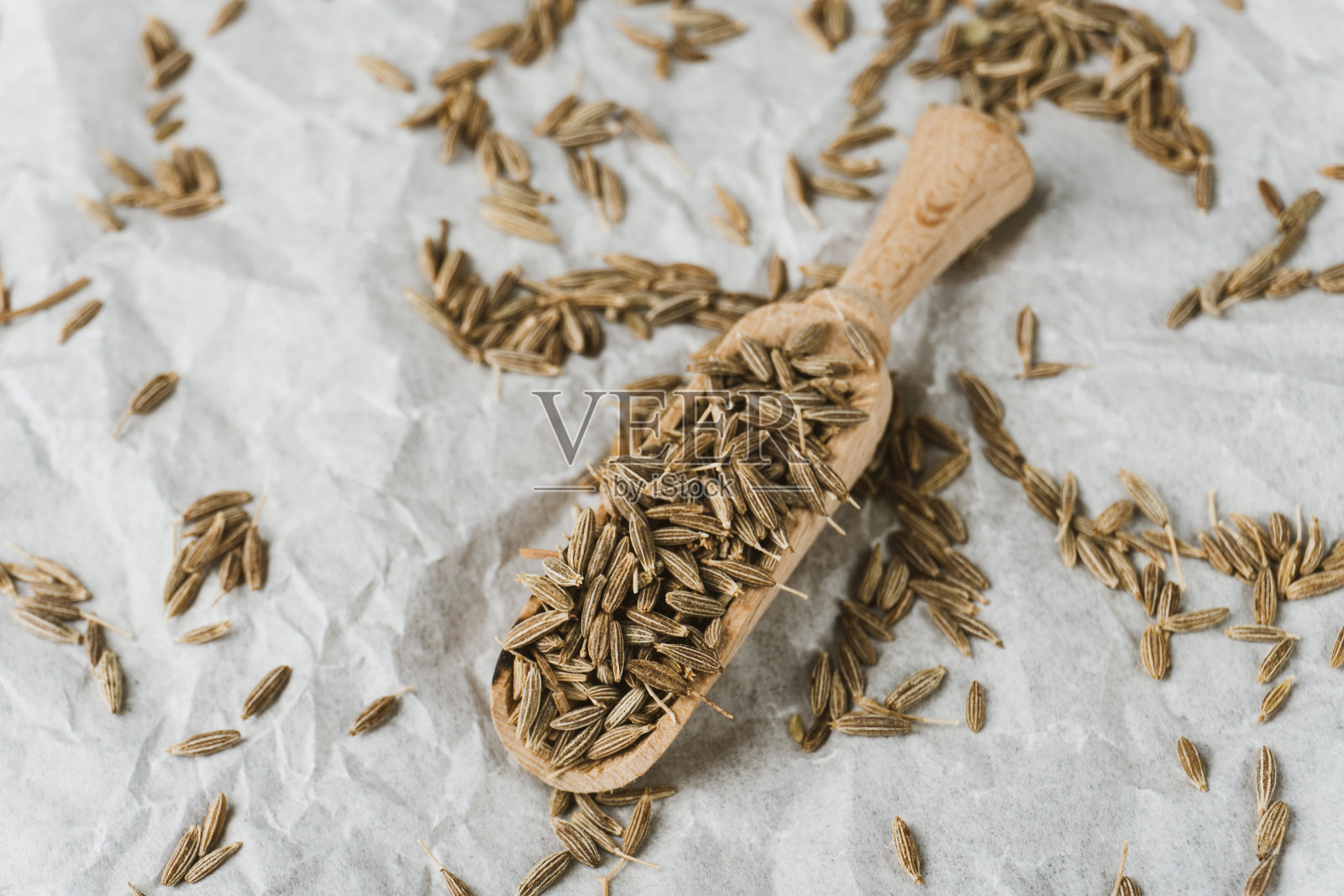 用木勺装干的小茴香籽，旁边放一堆齐拉，放在皱褶的白色纸上。俯视图照片摄影图片