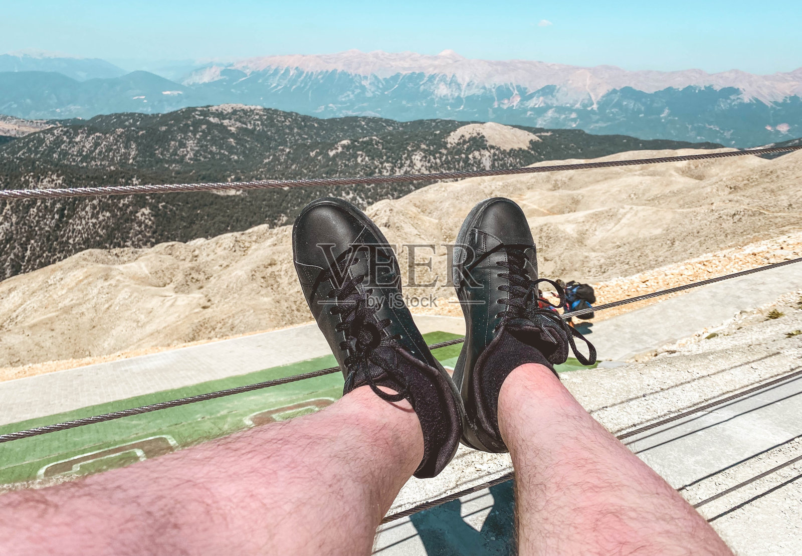 穿着黑色真皮运动鞋的男性腿。由天然材料制成的鞋。双脚从高处踩在山的背景上照片摄影图片