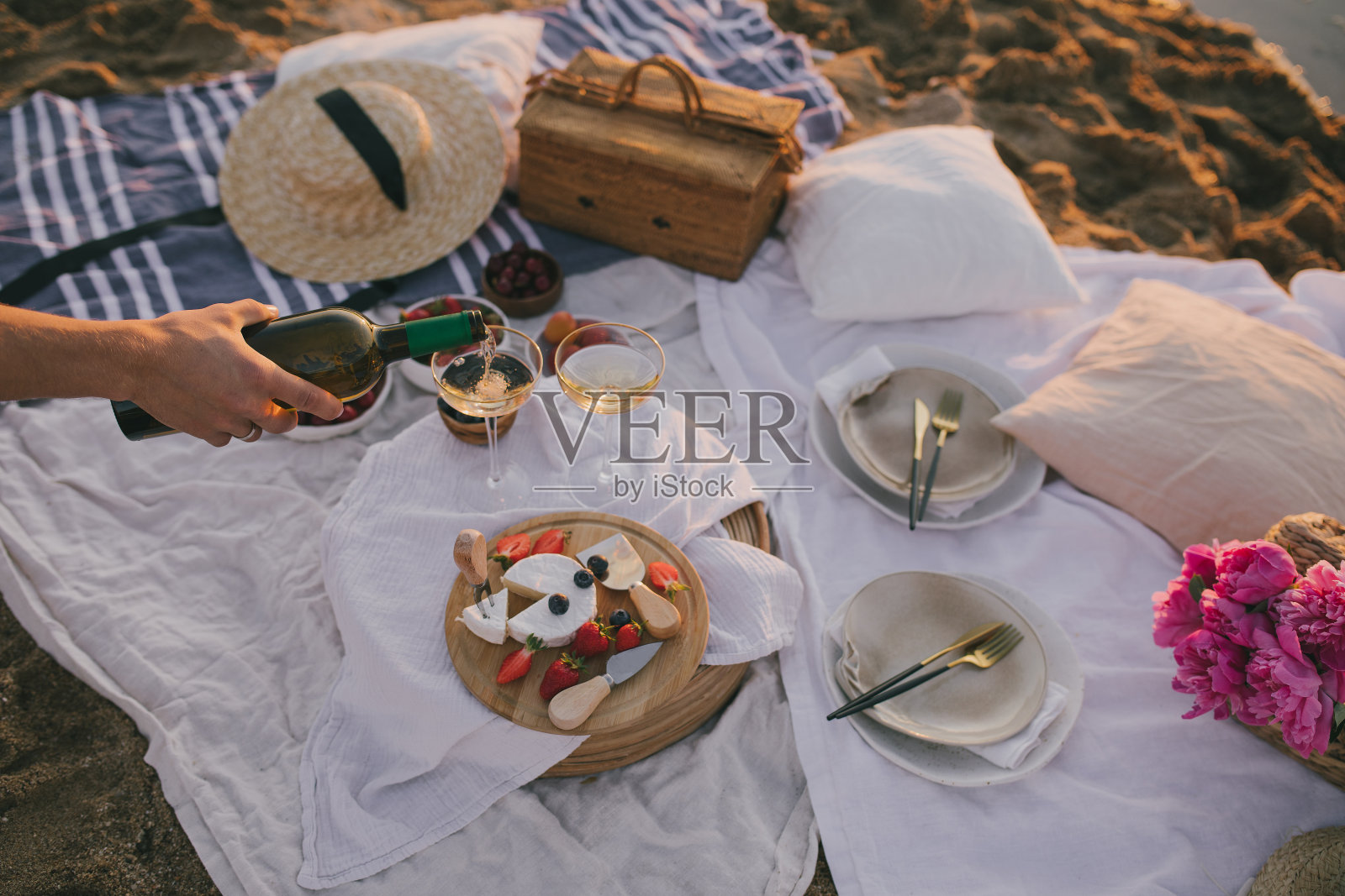 美丽浪漫的野餐，两杯白葡萄酒，新鲜的奶酪和浆果在日落的海滩上。照片摄影图片