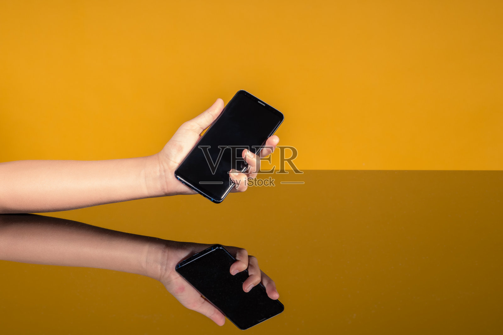 一个女人的手拿着一个手机在一个镜子桌子上反射。利用手机应用、通讯的概念，新款手机机型照片摄影图片