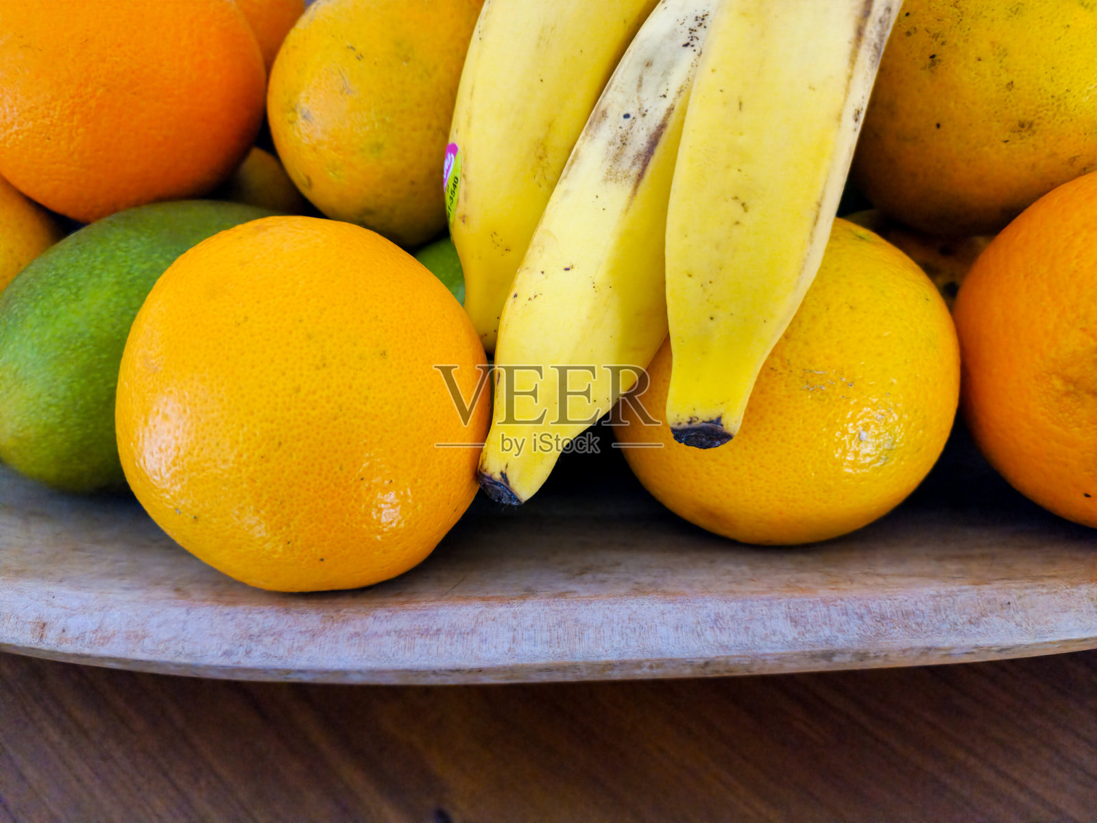 木桌上的水果碗里放着橙子、香蕉和芒果照片摄影图片