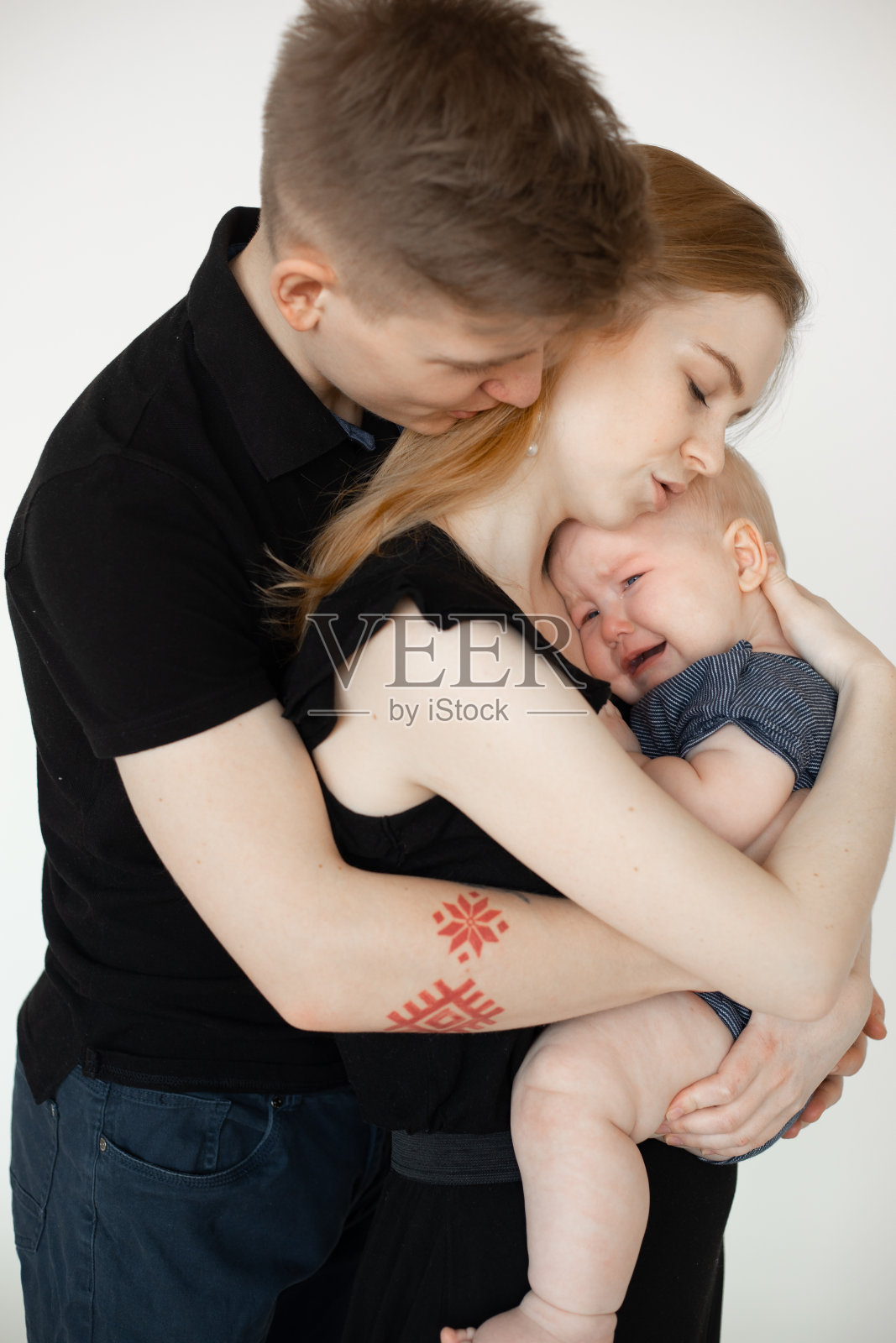 年轻美丽的家庭肖像在黑色的衣服与胖乎乎的娃娃脸婴儿婴儿蹒跚学步站在白色的背景。照片摄影图片