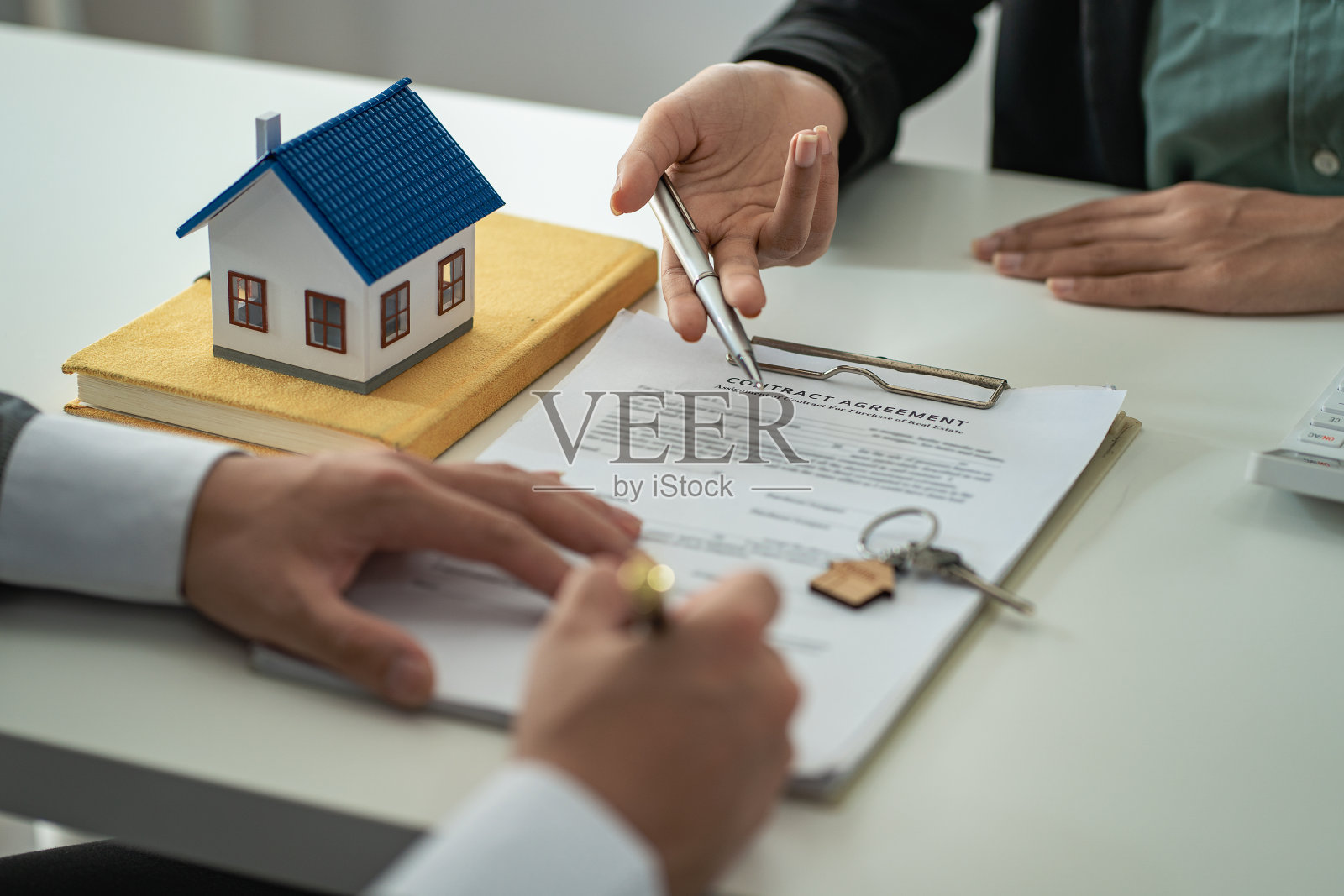 房地产经纪人讨论购房合同的条款，并要求客户签署文件，以合法地签订合同。在办公桌上卖房子的想法照片摄影图片
