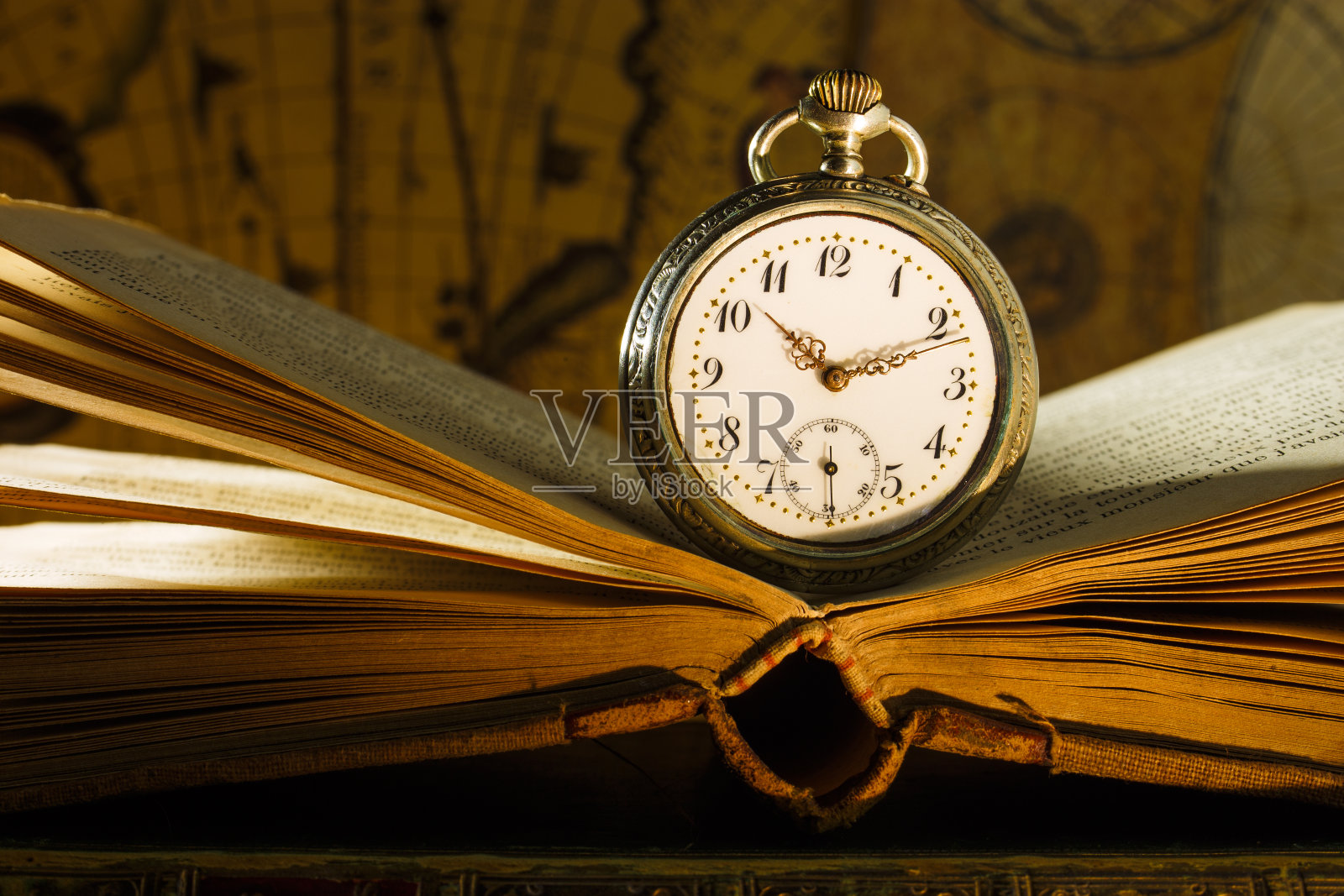 古董怀表放在打开的旧书上。背景是旧地图。照片摄影图片