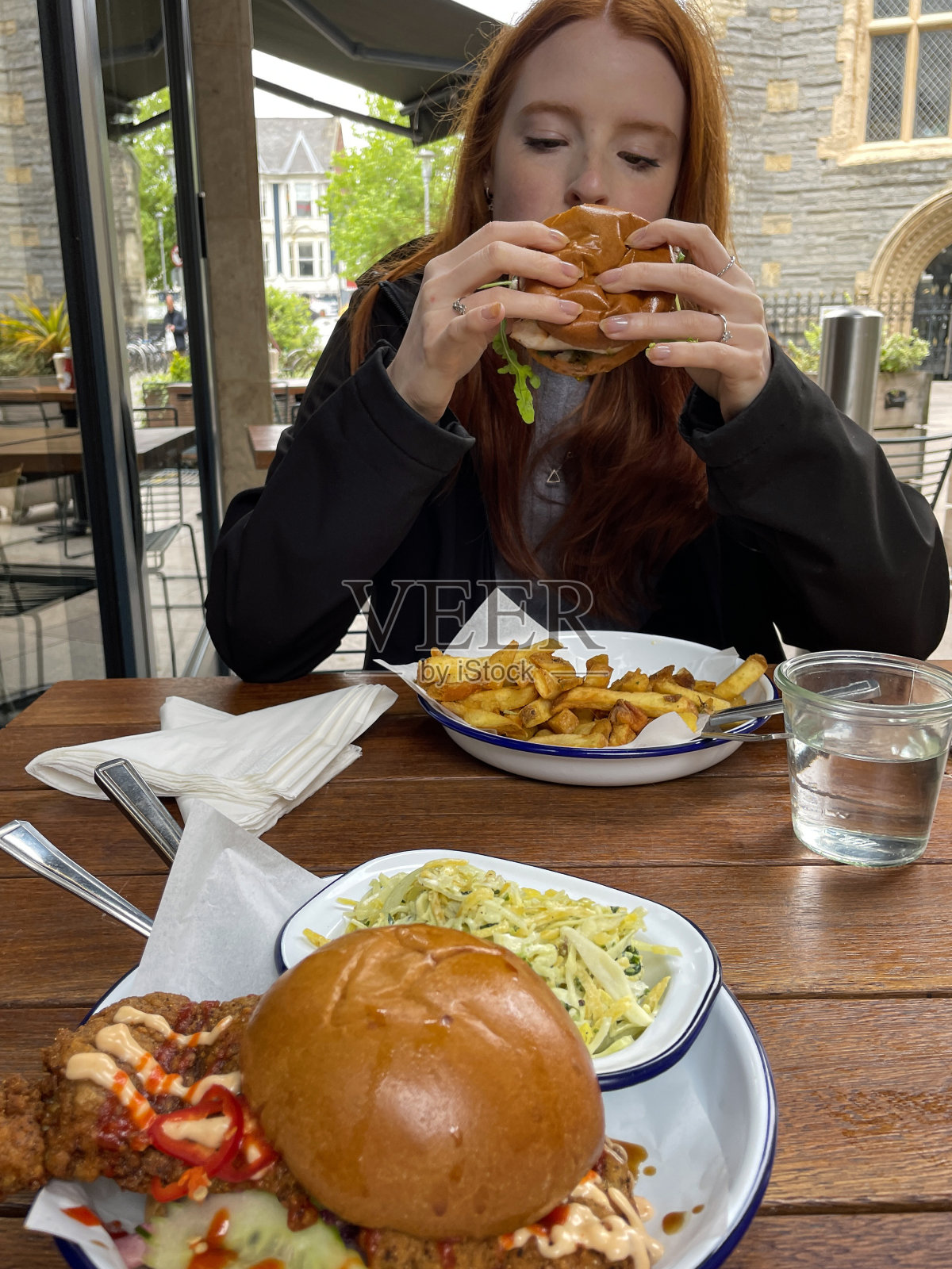 迷人的形象，红头发，年轻女子拿着美食，鸡肉香蒜沙司汉堡准备咬，面包面包与鸡胸肉，火箭，牛肉番茄片，餐厅的场景，重点放在前景照片摄影图片