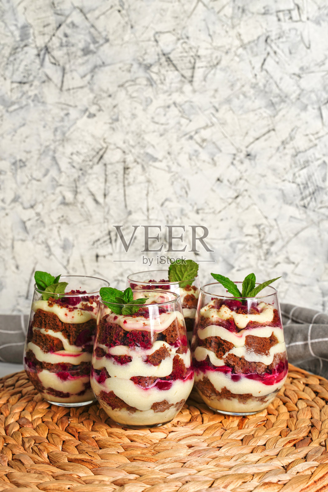 四个透明的杯子，配上棕色巧克力和白色奶油的甜点。蛋糕用薄荷叶装饰，这是生日蛋糕。照片摄影图片