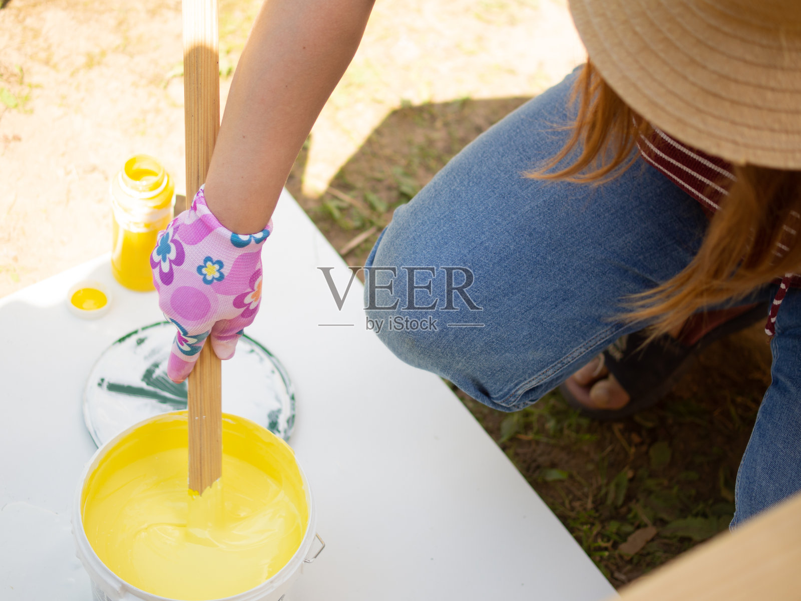 少女画家混合黄色和白色油漆，混合颜色丙烯酸门面漆。油漆在桶中混合照片摄影图片