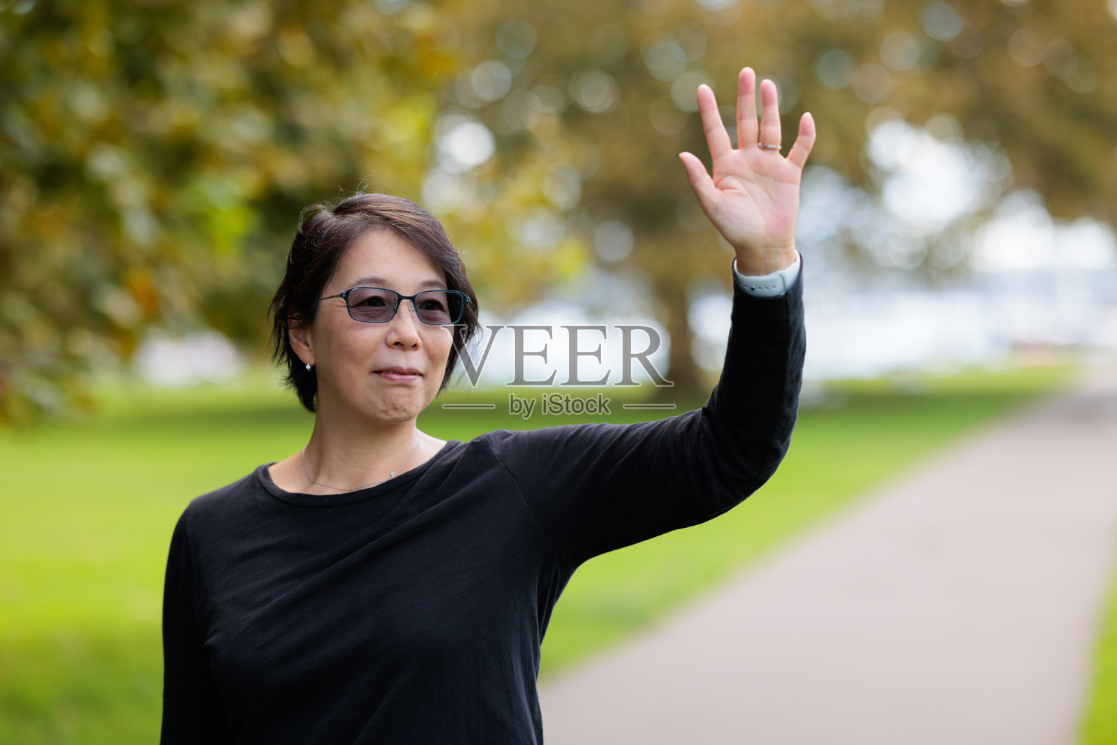 公园里微笑的女人在挥手。照片摄影图片