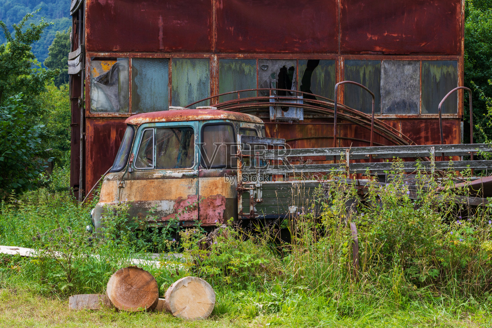 在森林的边缘，一辆锈迹斑斑的静止不动的旧汽车停在一间锈迹斑斑的铁皮棚子旁。照片摄影图片