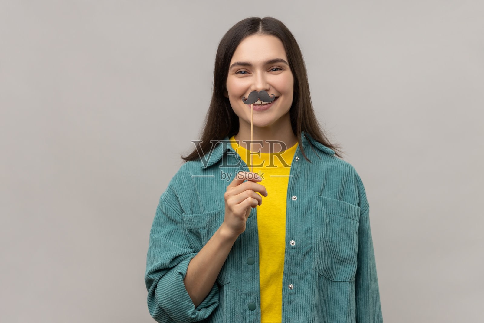 深色头发的女人站在纸胡子粘上，节日的心情，假面舞会。照片摄影图片