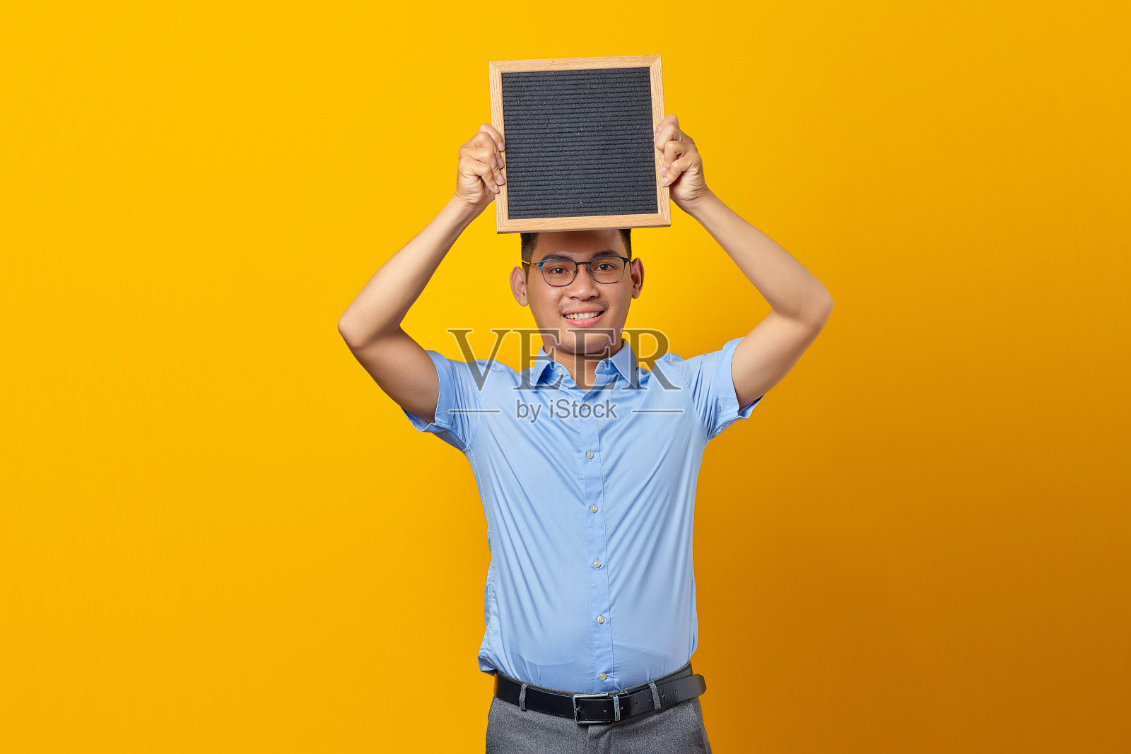 肖像微笑的年轻亚洲商人在眼镜拿着黑板，自信地看着相机孤立的黄色背景照片摄影图片