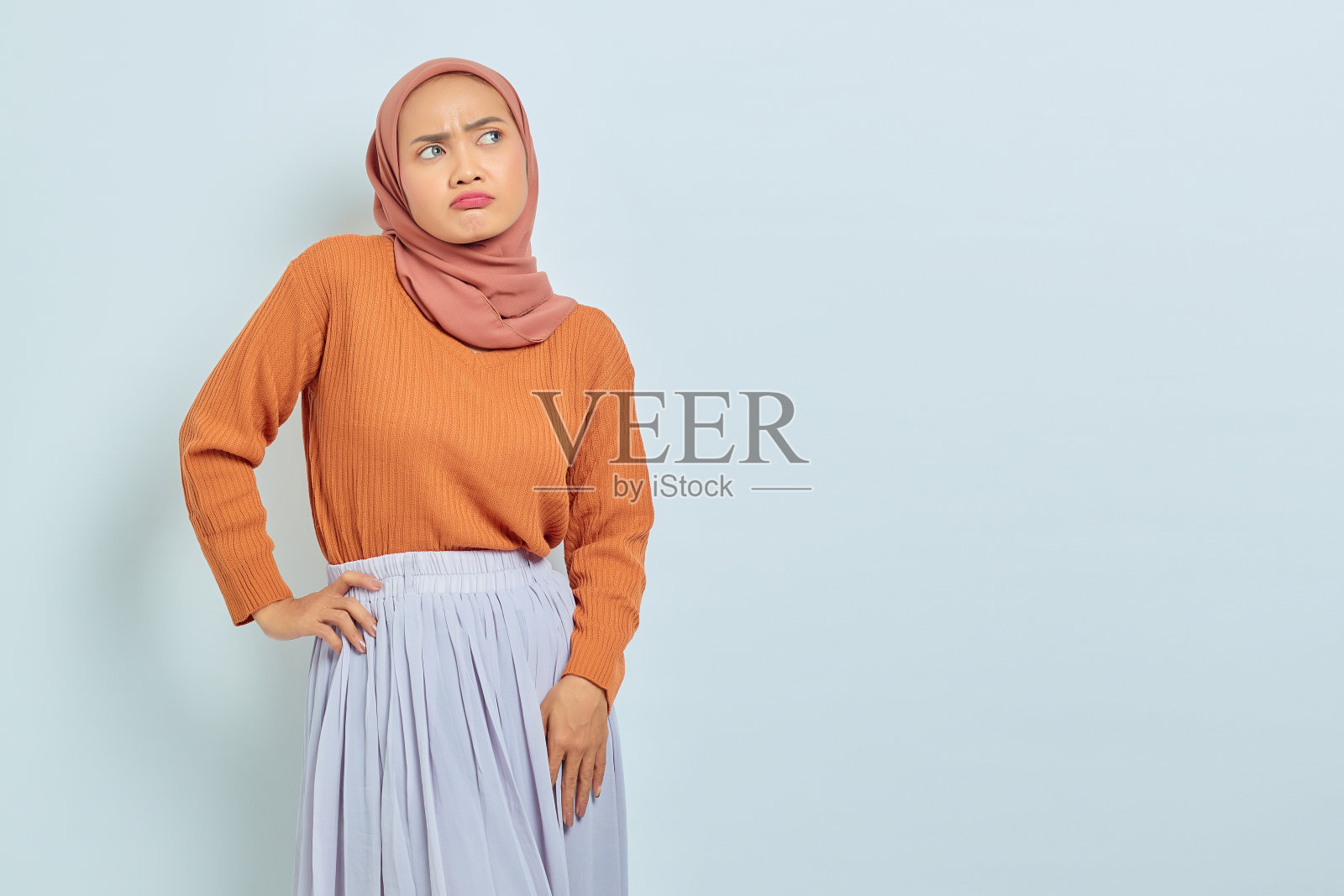 年轻美丽的亚洲穆斯林妇女肖像在棕色毛衣，站在困惑的表情和看着复制空间孤立的白色背景。穆斯林生活方式的概念照片摄影图片