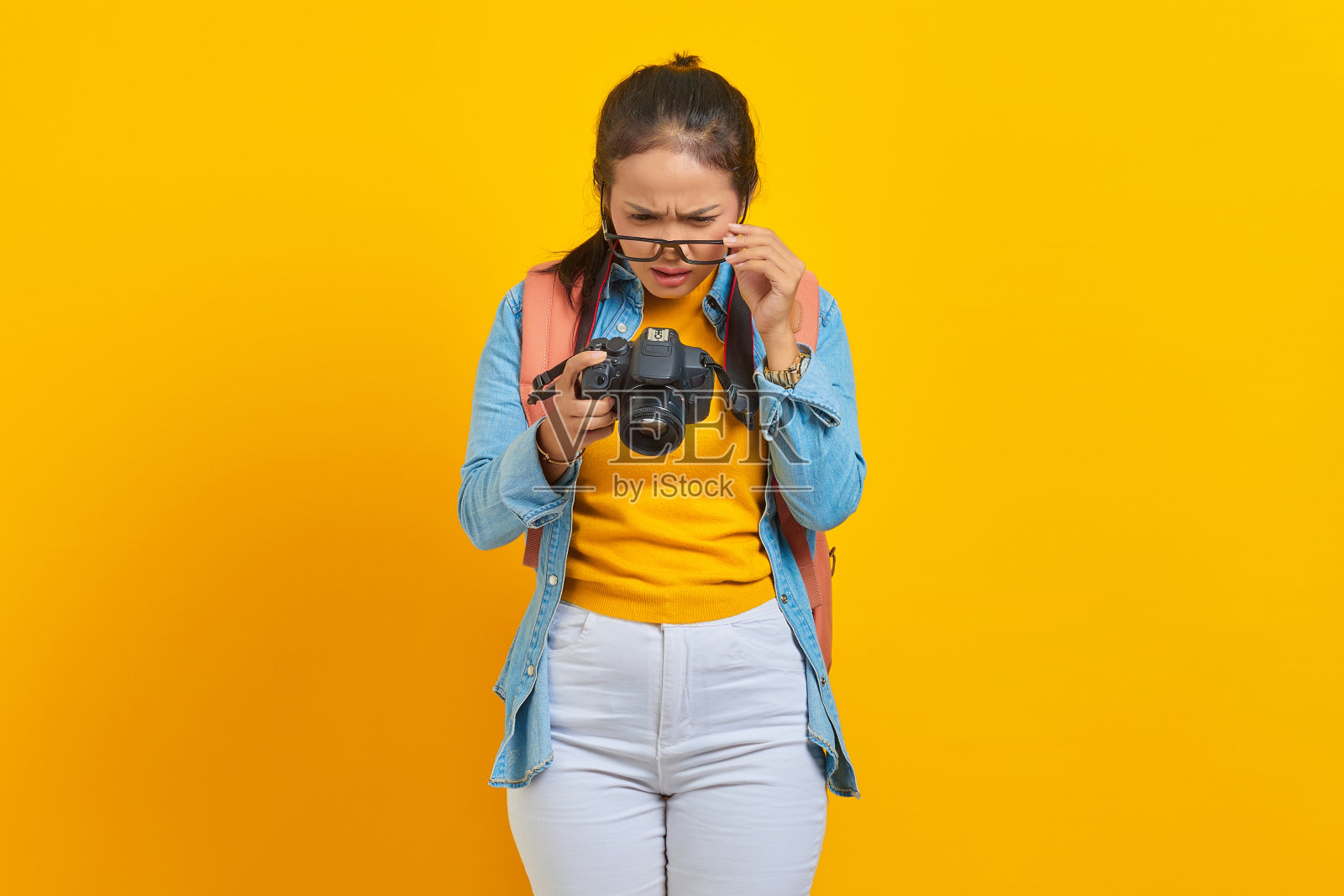惊讶的年轻亚洲妇女的肖像看着相机上的照片孤立的黄色背景。周末旅客出行。航空飞行旅程概念照片摄影图片