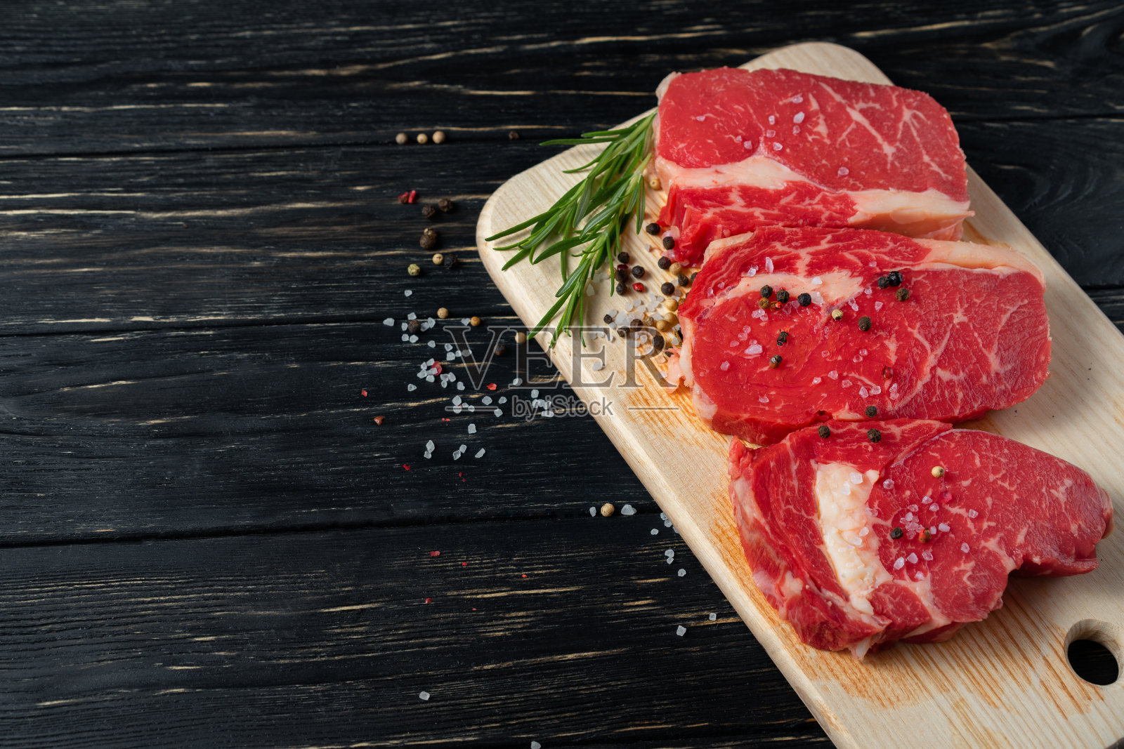 黑木桌上的砧板上放着三块多汁的生牛肉。照片摄影图片