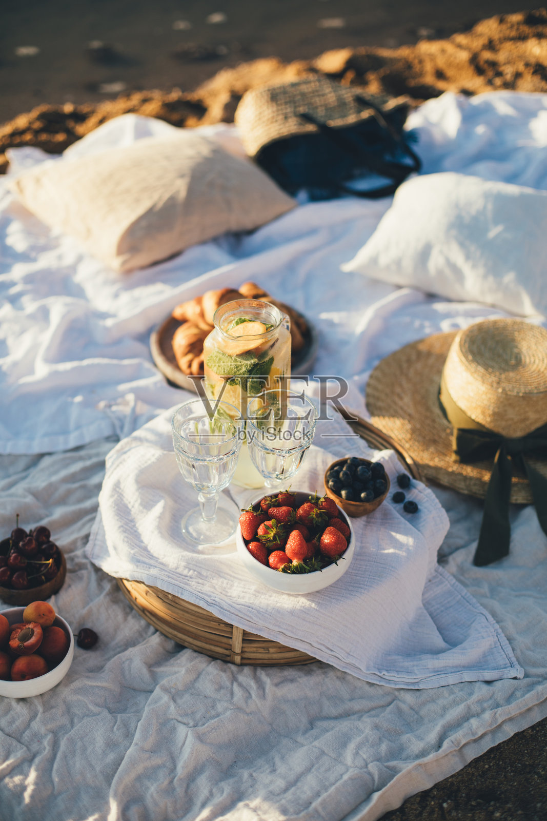 美丽的野餐，新鲜的水果，柠檬水和羊角面包在海滩上的日落。照片摄影图片