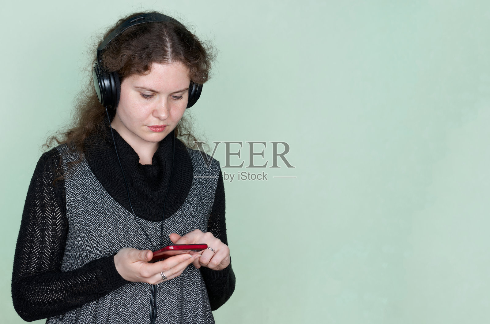 工作室拍摄的漂亮女人选择歌曲从播放列表使用智能手机和耳机。科技的生活方式照片摄影图片