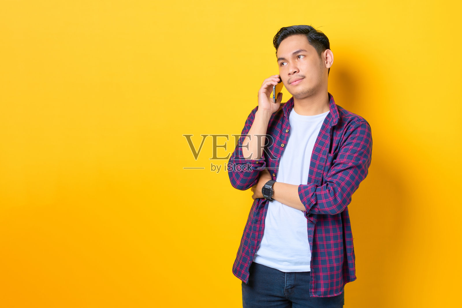 困惑的年轻亚洲男子在格子衬衫谈手机和看远离拷贝空间孤立的黄色背景照片摄影图片