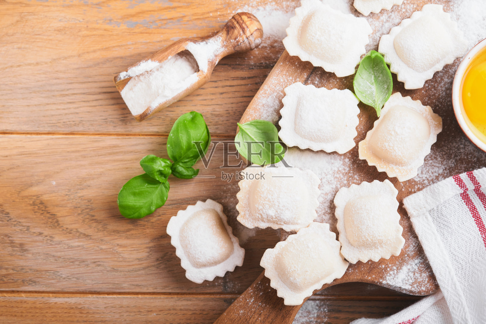 意式馄饨意大利菜。美味的自制意大利饺子，面粉，西红柿，鸡蛋和绿色罗勒在木制背景。意大利馄饨的制作过程。烹饪食材背景。前视图。照片摄影图片