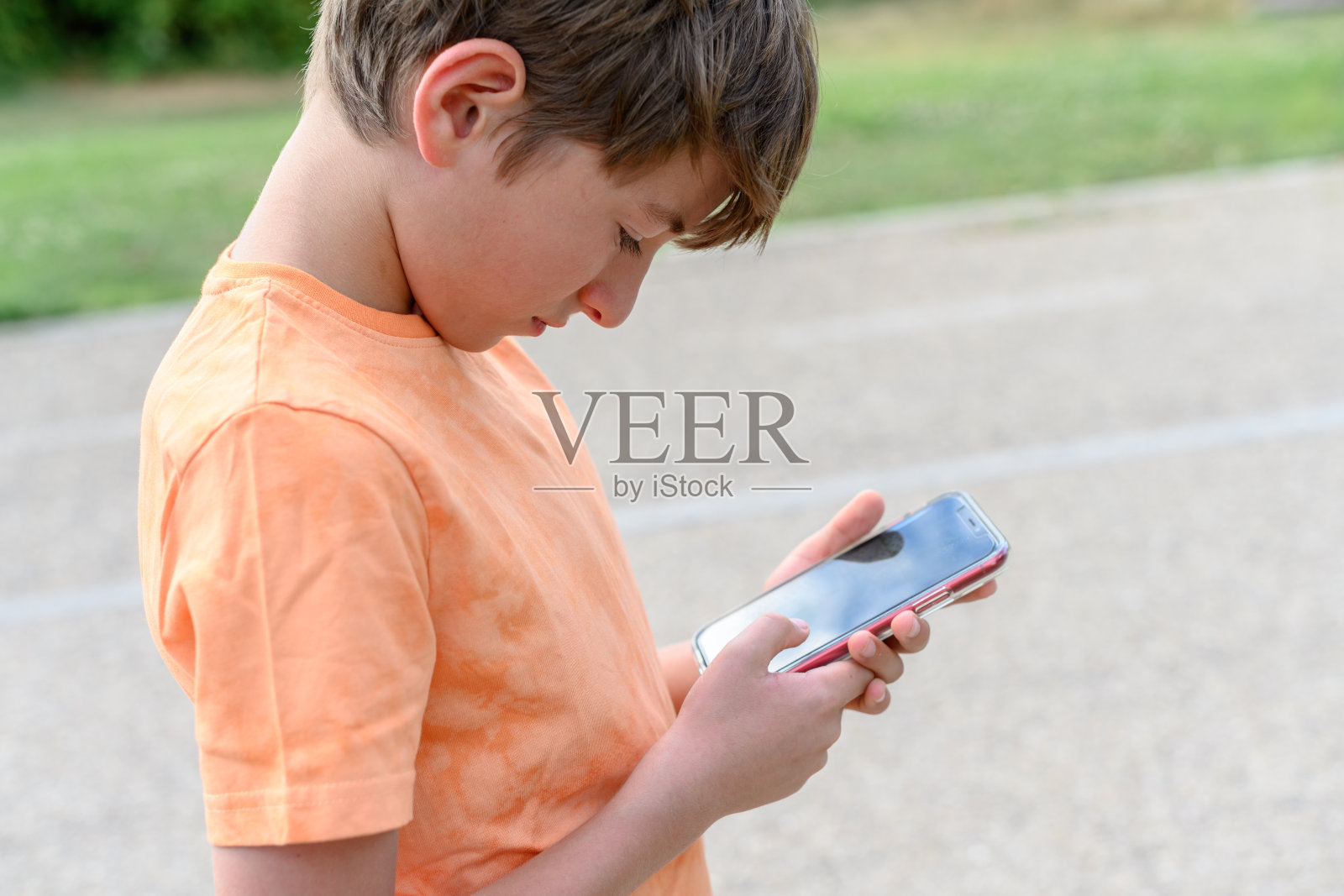 一个不到十岁的男孩在街上看手机自娱自乐。对技术上瘾的概念照片摄影图片