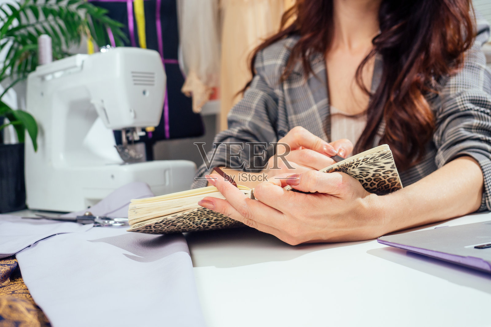 漂亮的长头发女裁缝在笔记本上写着。裁缝制作了一系列服装。年轻女子设计师的衣服笔记想法照片摄影图片