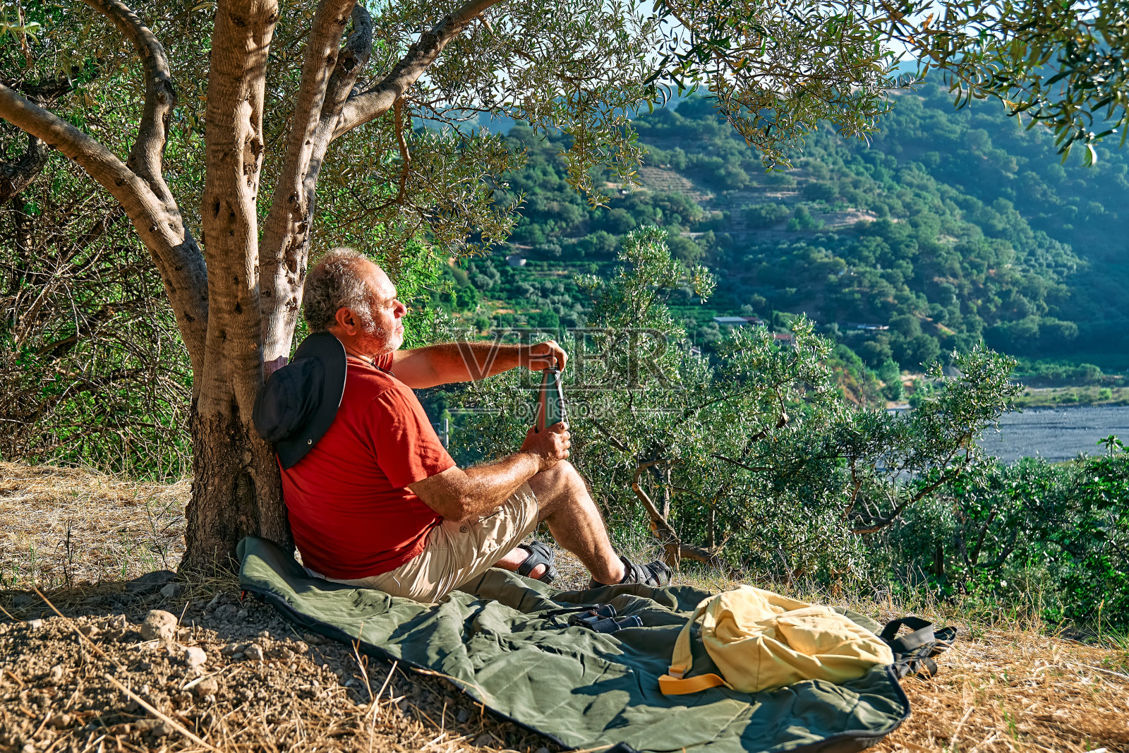 游客在橄榄树林里休息，喝热钢瓶里的水，旅行或户外运动。积极的人，远足，健康的生活方式和和谐的理念。与自然统一。照片摄影图片