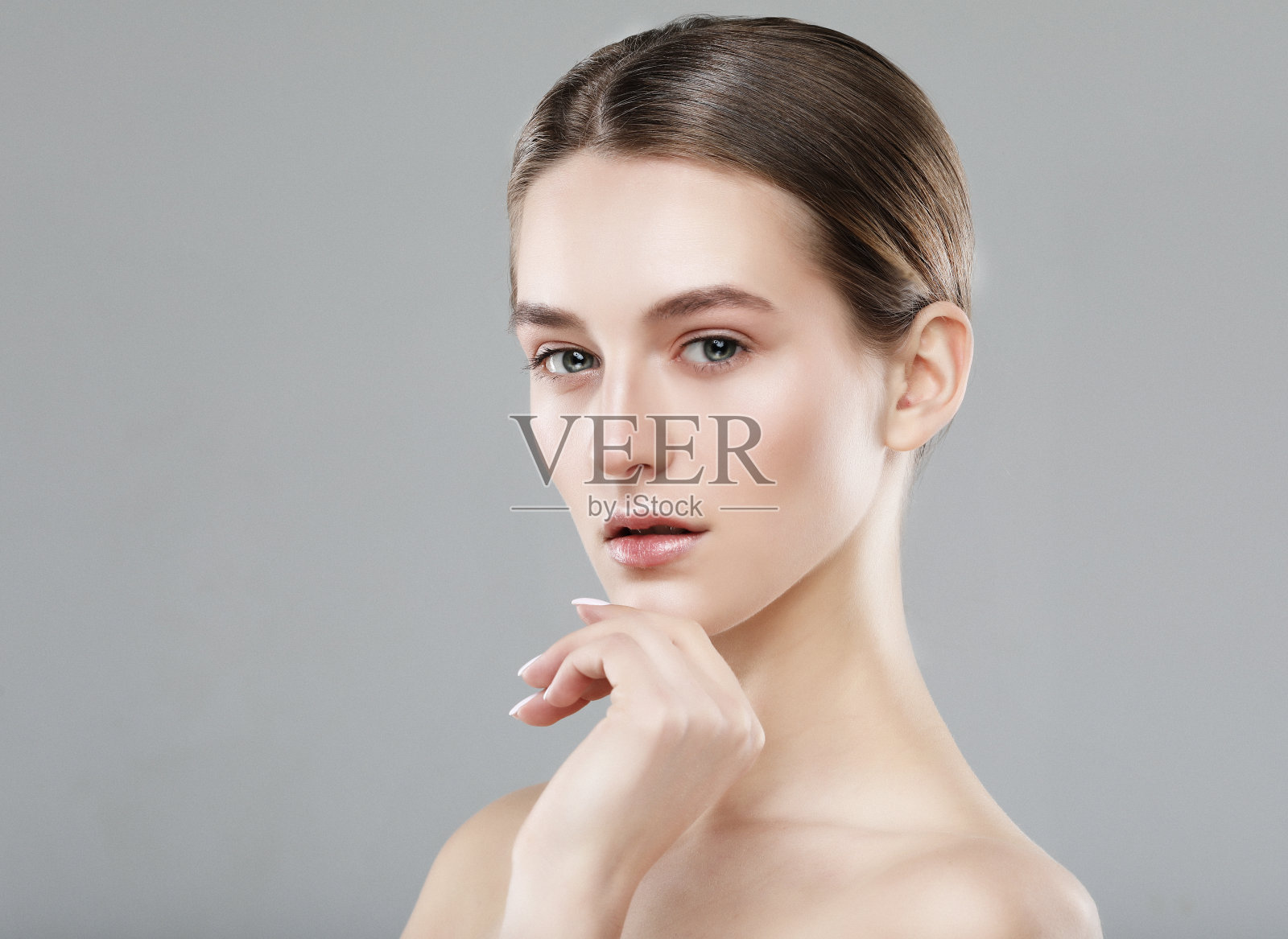 美丽的年轻女子与清洁新鲜的皮肤触摸她的脸在灰色的背景。照片摄影图片
