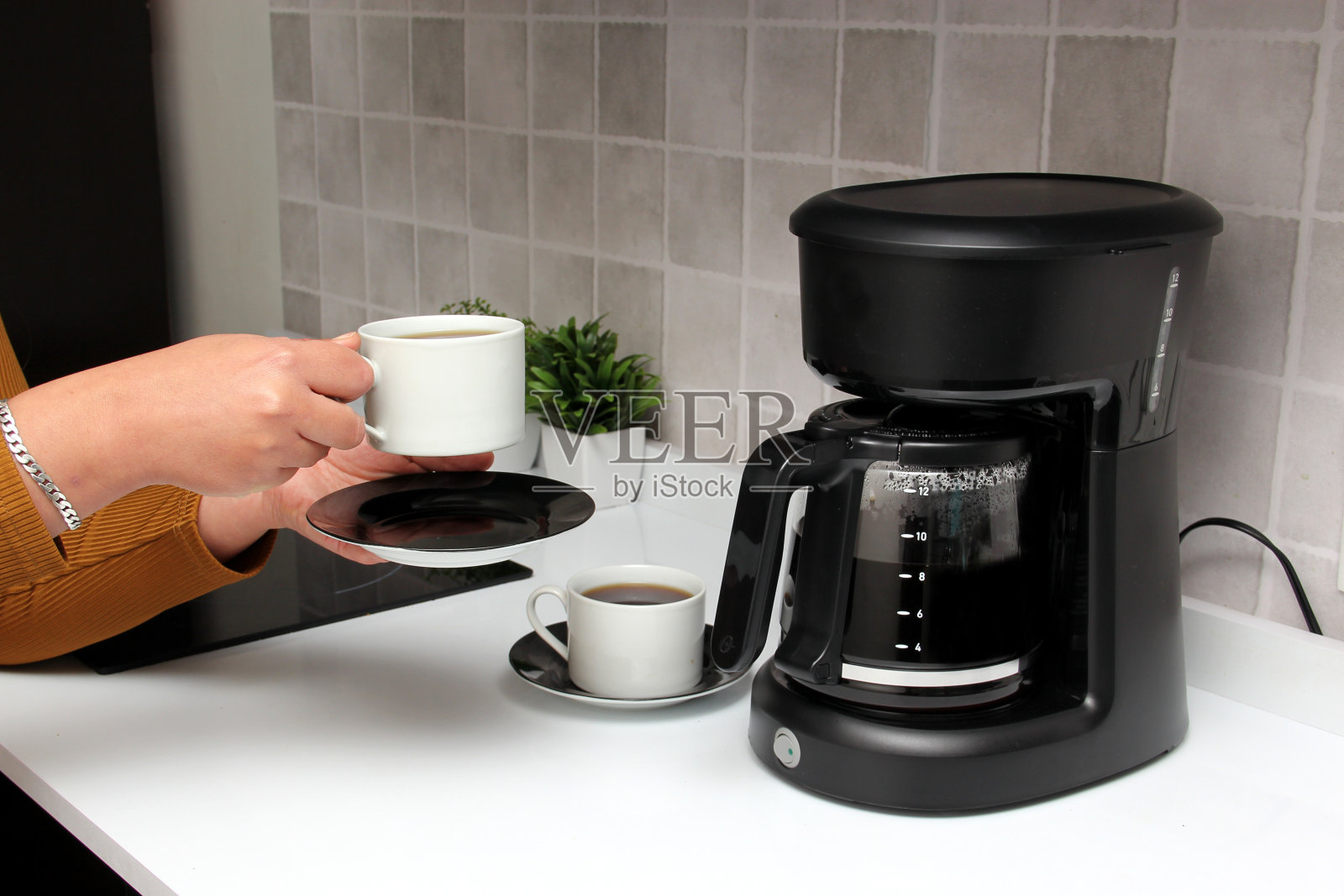 女人的手端着咖啡机煮好的咖啡开始新的一天，它含有抗氧化剂，可以预防癌症，对抗阿尔茨海默病和帕金森病照片摄影图片