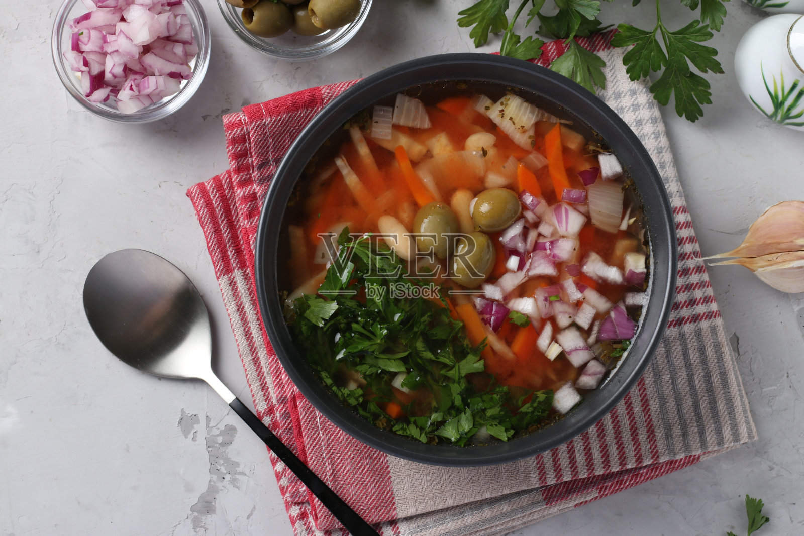 希腊西红柿汤，蔬菜，橄榄和白豆在一个黑色的碗里，灰色的背景。前视图。照片摄影图片