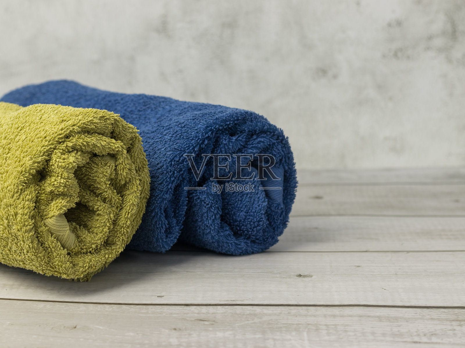 浴室的木桌上放着卷好的毛巾，蓝色和绿色的照片摄影图片