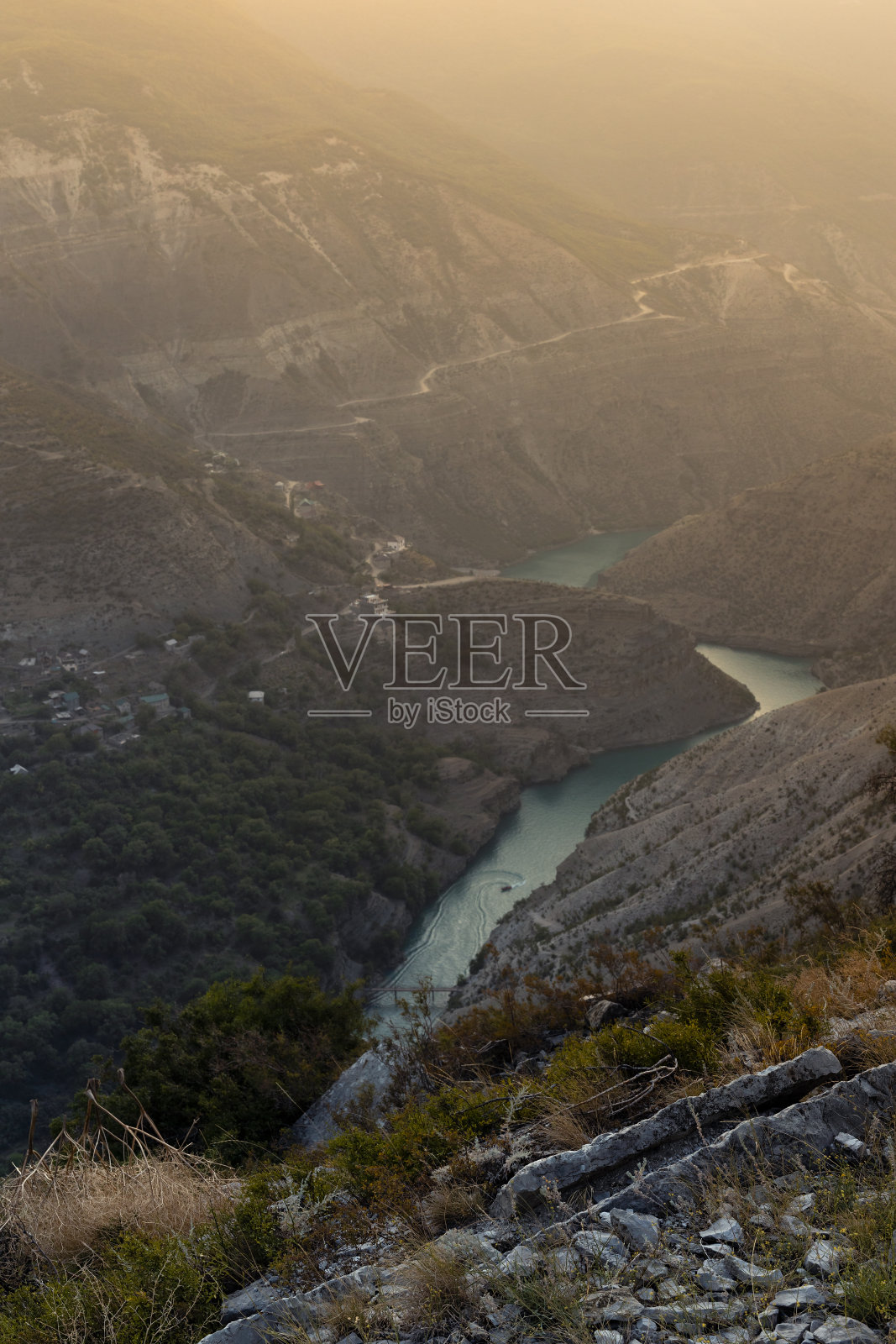 山脉全景景观——深邃的峡谷与陡峭的山坡，薄蓝色的河流，船，蛇形的道路在夕阳下金色的阳光，柔雾，垂直。徒步旅行，旅游，野外旅行。照片摄影图片