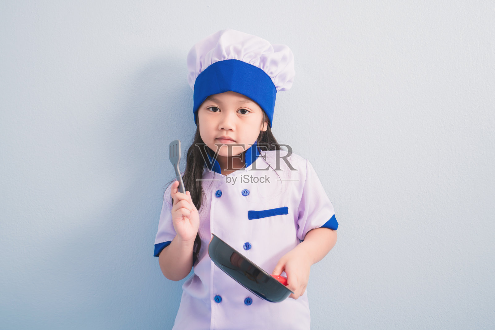 穿着衣服，戴着厨师帽的快乐女孩，梦想着成为一名厨师照片摄影图片