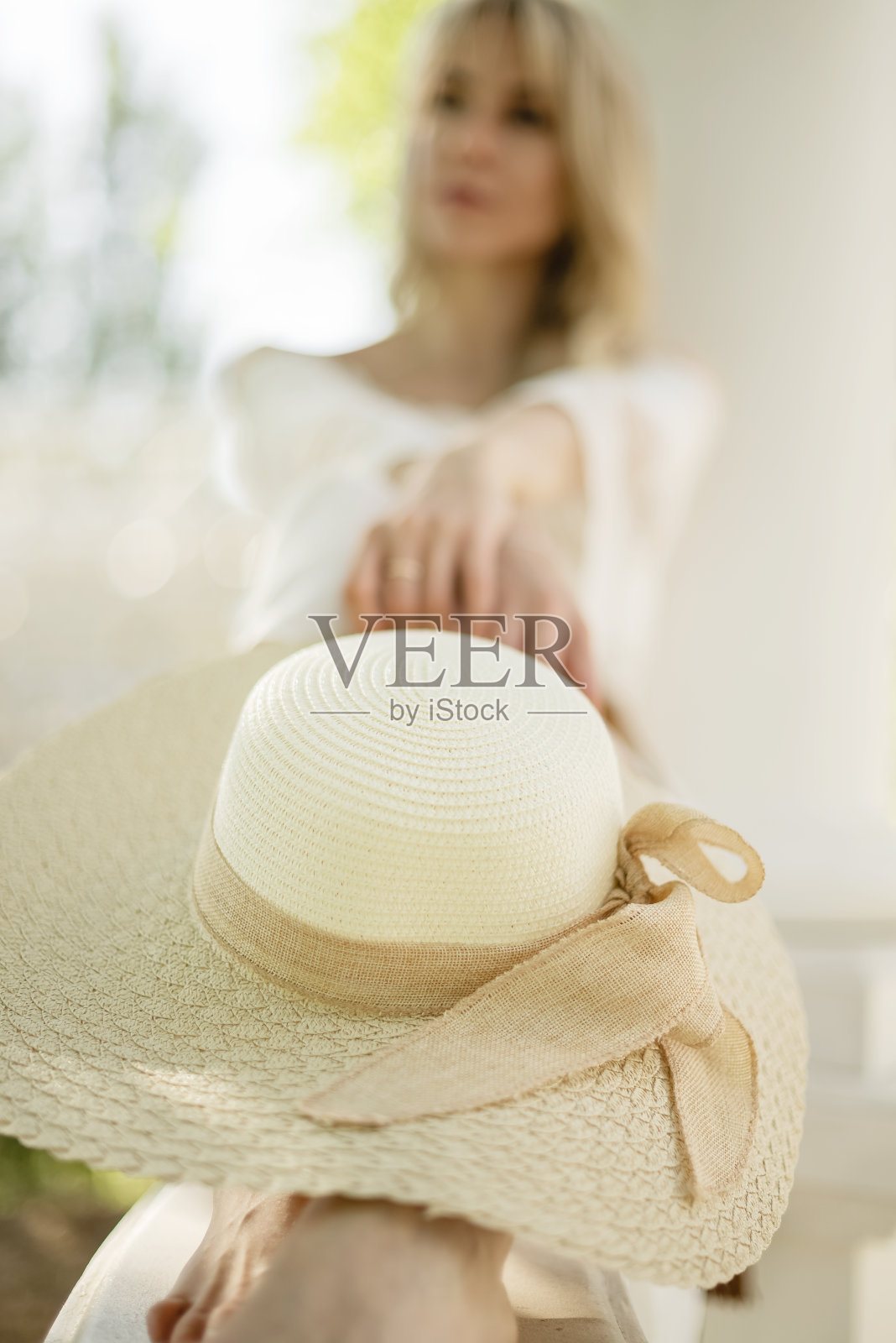 一名白衣女子坐在室外的走廊上，膝盖上戴着草帽照片摄影图片