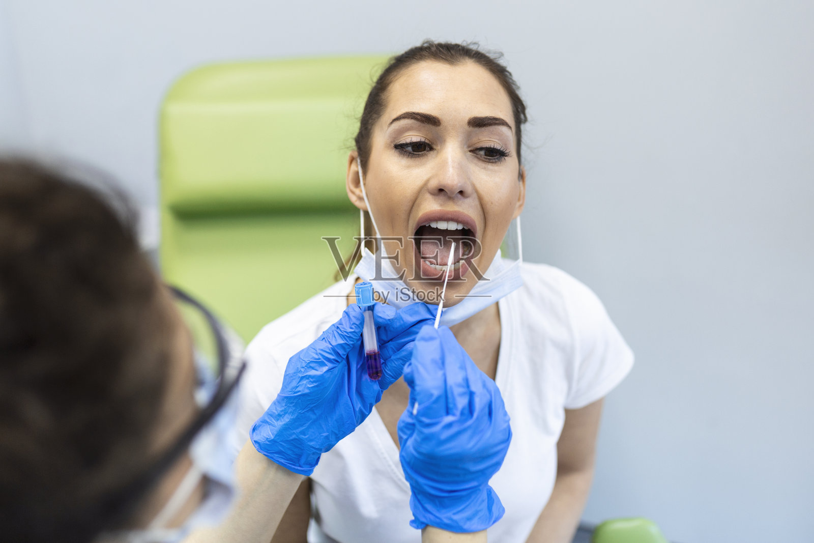 医生对女病人进行咽拭子化验。医务工作者穿着防护服。他们在流行病期间住院。照片摄影图片