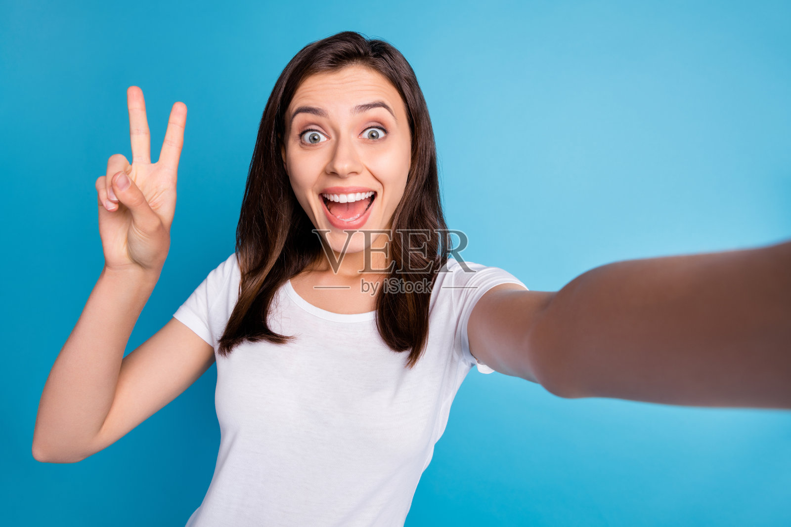 年轻快乐开朗积极微笑的女孩的照片自拍显示v标志孤立在蓝色的背景照片摄影图片