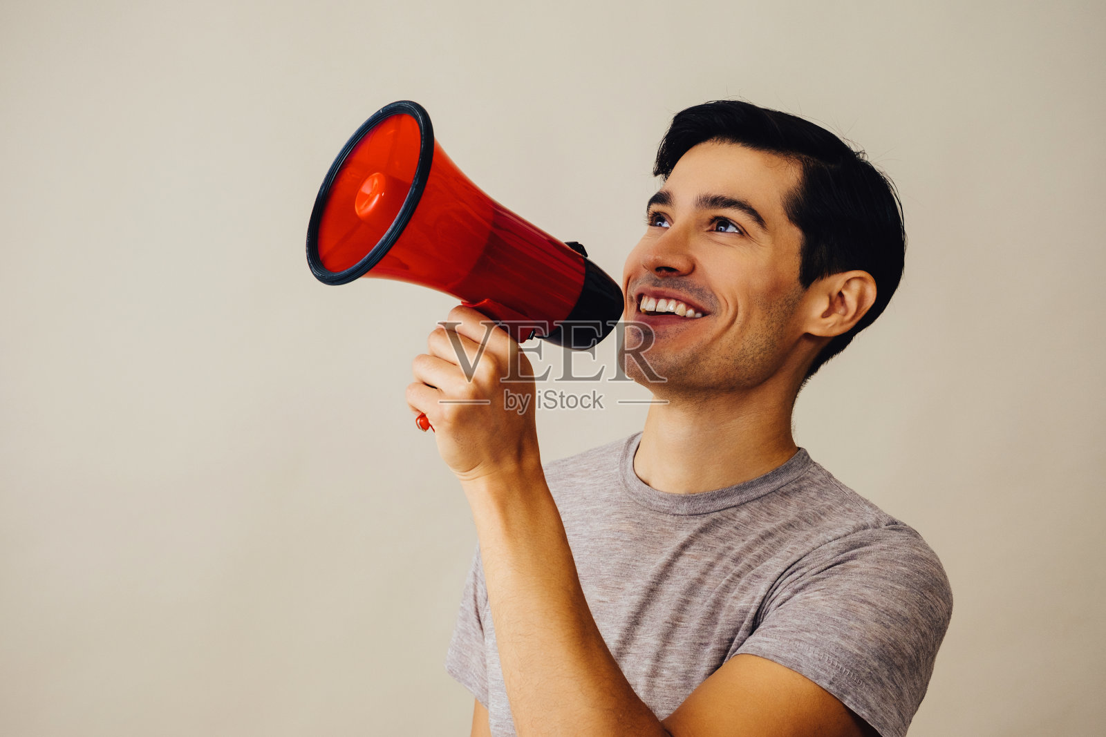 肖像西班牙裔拉丁裔男子拿着红色扩音器微笑英俊的年轻人灰色t恤看着远处的拷贝空间照片摄影图片