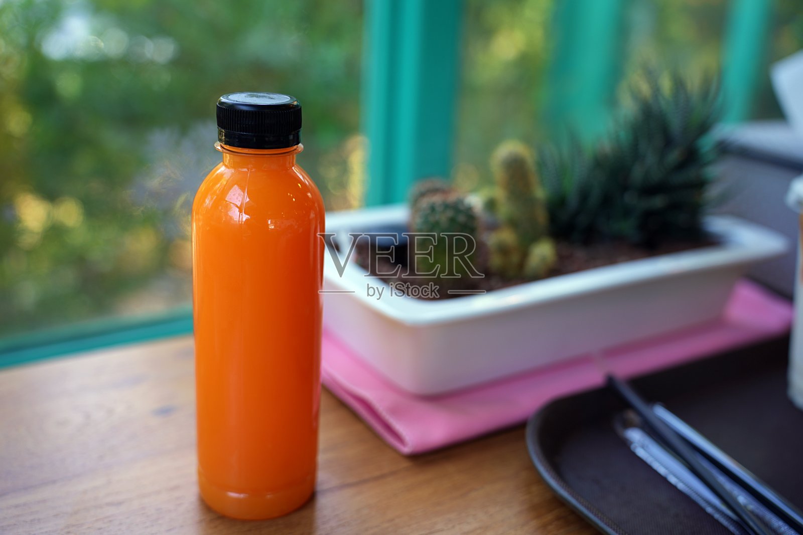 鲜榨的橙汁装在瓶子里，果汁凉下来，仙人掌树模糊背景照片摄影图片