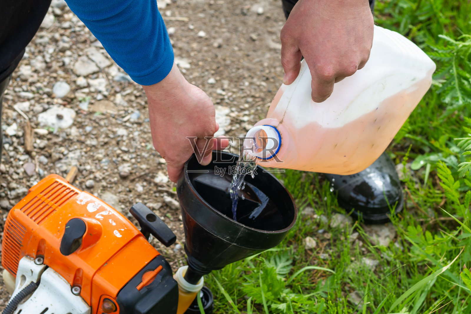 一名男子用塑料油箱给割草机的汽油发动机加油照片摄影图片