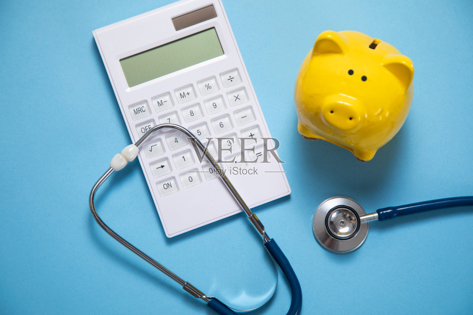 蓝色背景的带听诊器和计算器的存钱罐。照片摄影图片