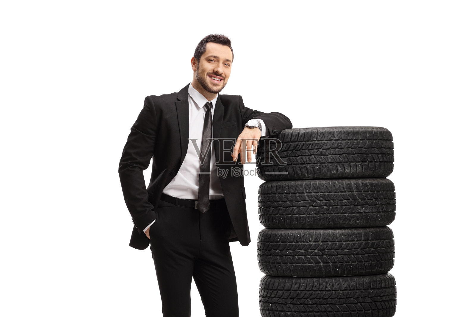 西装革履的男人倚在一堆汽车轮胎上照片摄影图片